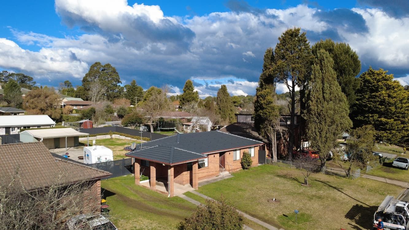 Aerial view of suburban homes with brick exteriors, green lawns, and trees under a cloudy sky.