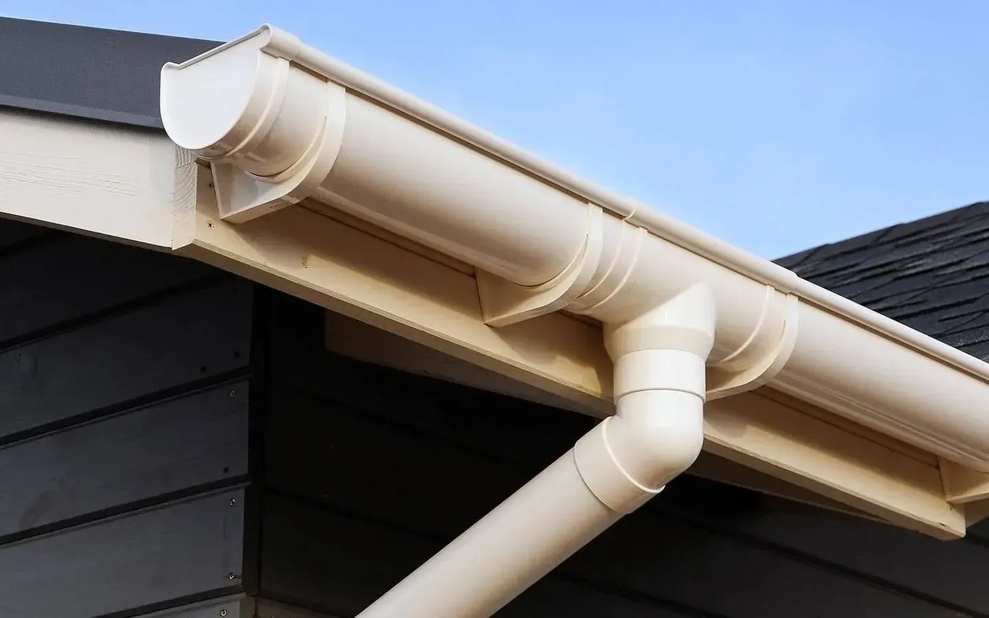 Rain gutter and downspout on a house roof against a blue sky