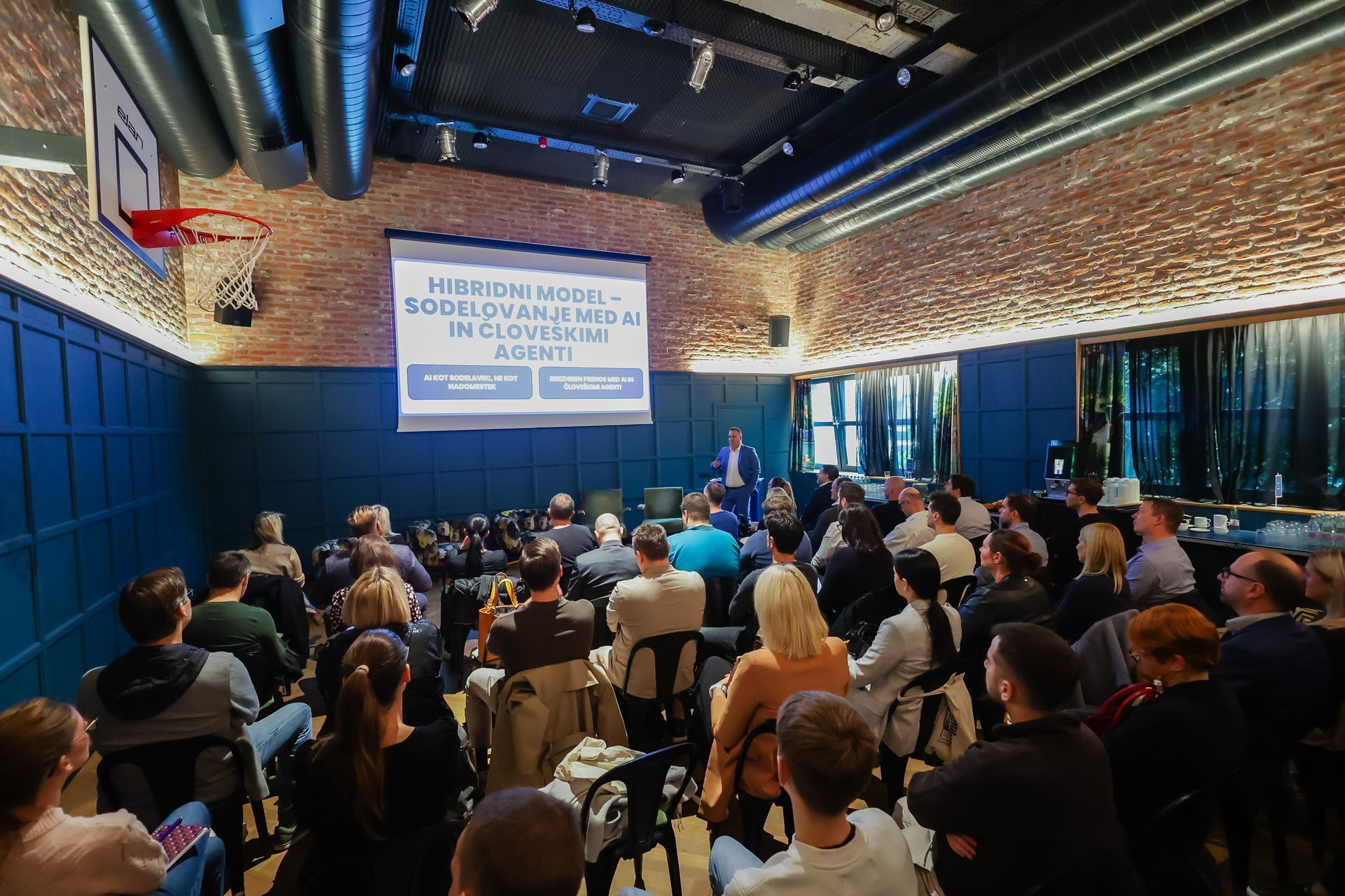 Public at an event. Speaker infront of them. Blue background.