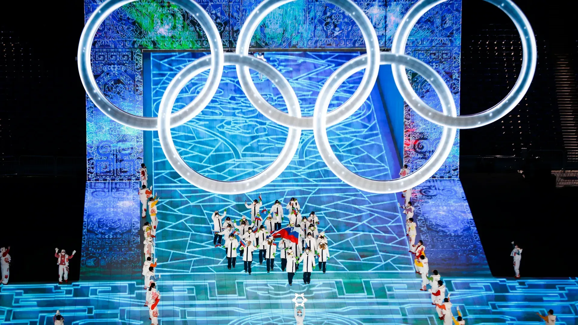 Športniki v belo-modrih uniformah korakajo pod olimpijskimi krogi med slovesnostjo na olimpijskih igrah v Pekingu.
