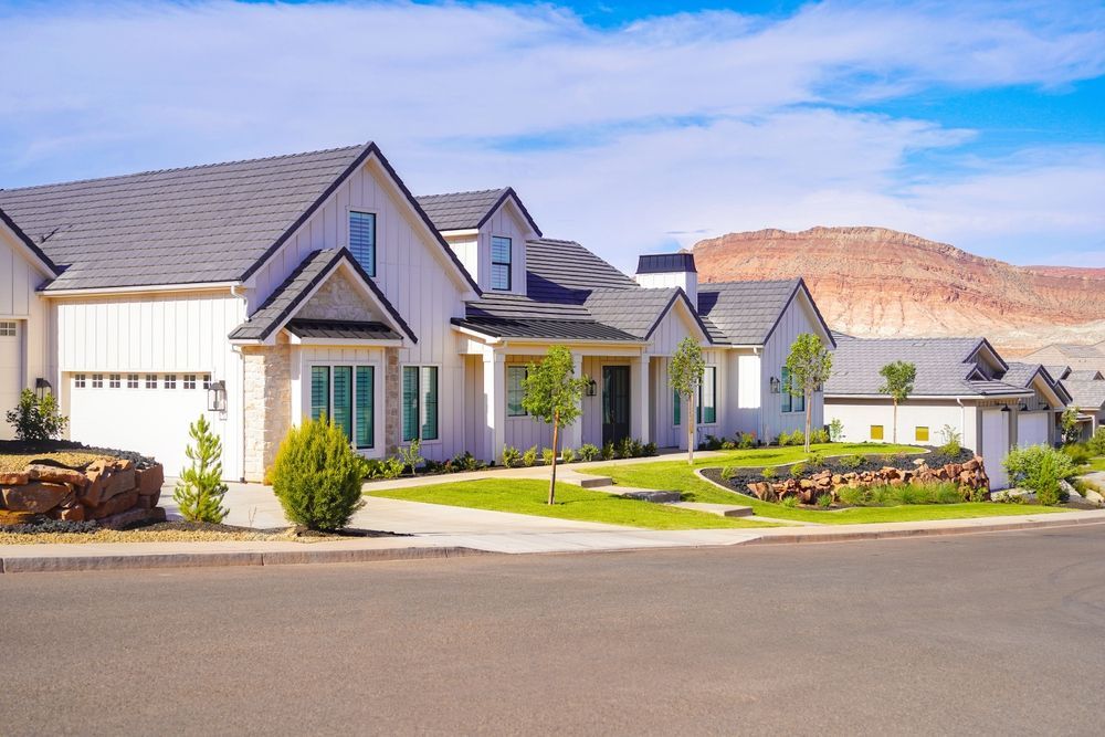 Modern white suburban homes with gray roofs under a blue sky, set against a distant red rock mountain landscape.