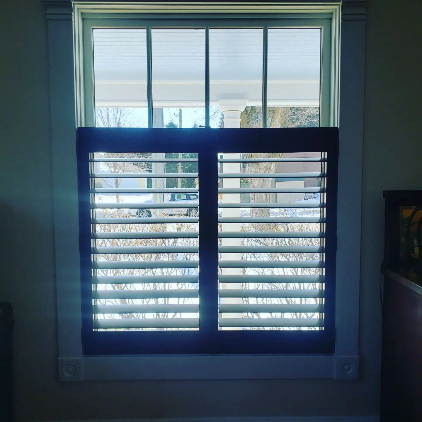 A window with white blinds partially open, showing a snowy outdoor view.