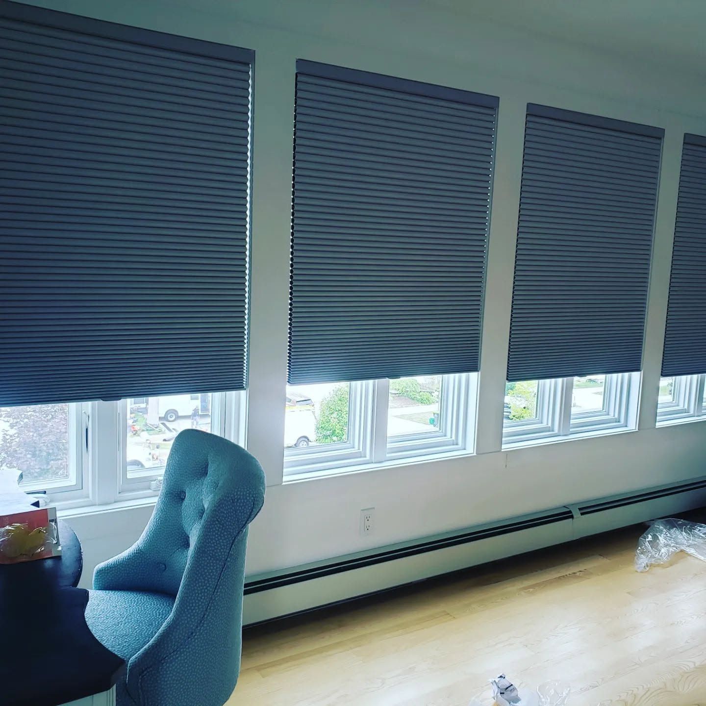 Blue blinds over windows in a bright room with a blue chair and hardwood floor