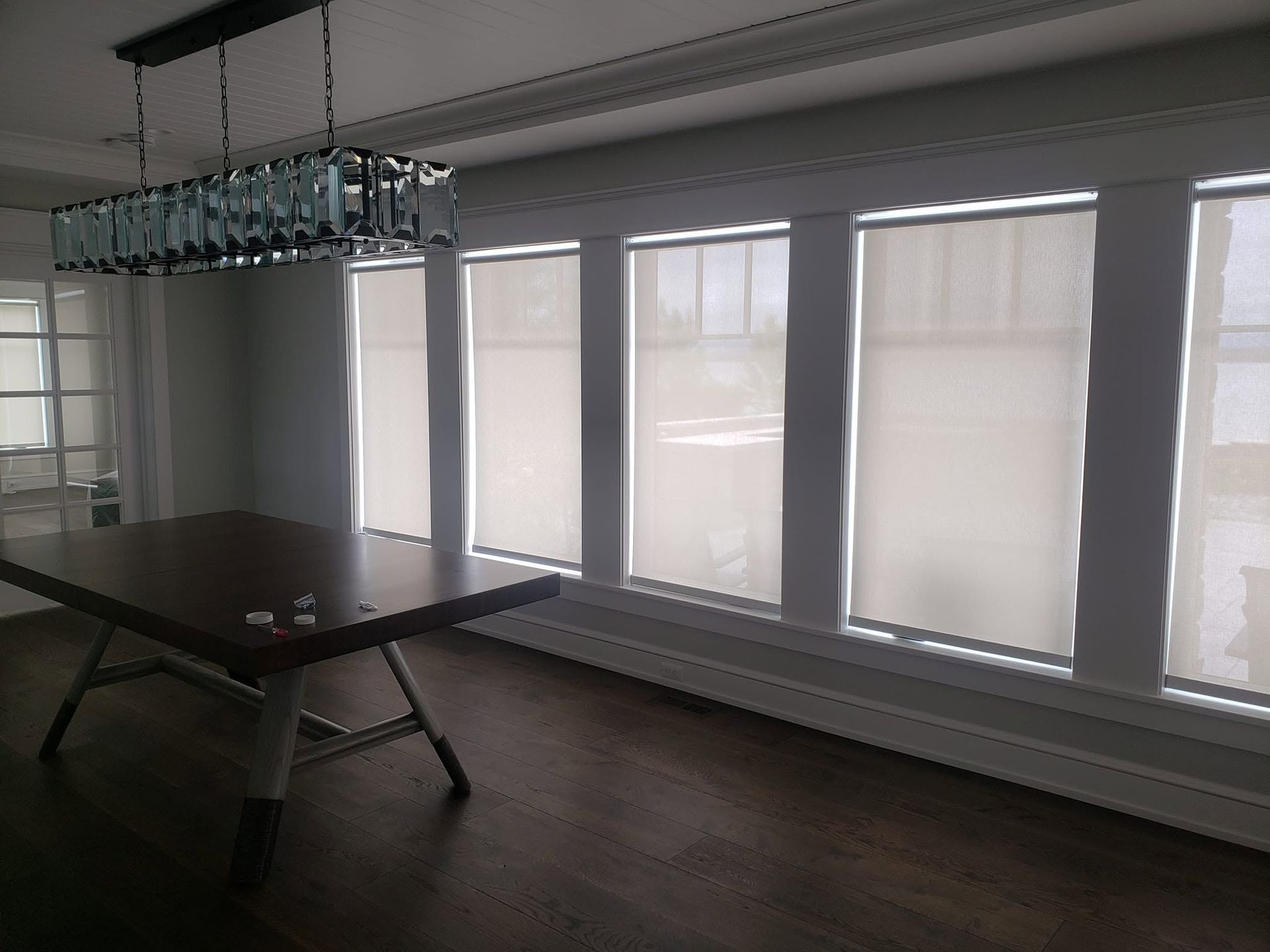 Empty meeting room with a large table and hanging light fixture beside tall windows with blinds