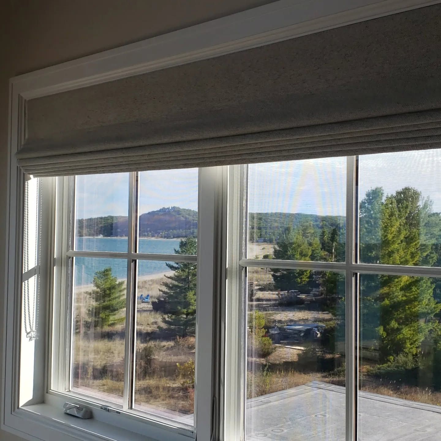 Sunlit window view of a blue lake, distant hills, and trees with closed blinds above the panes