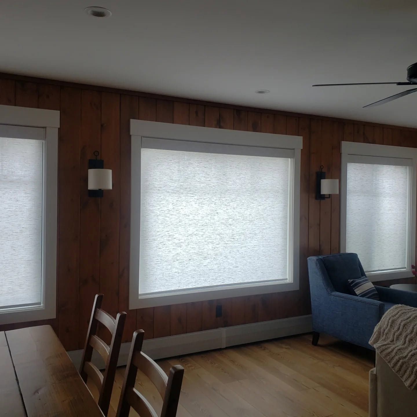 Wood-paneled living room with large windows, dining table, and blue chaise lounge