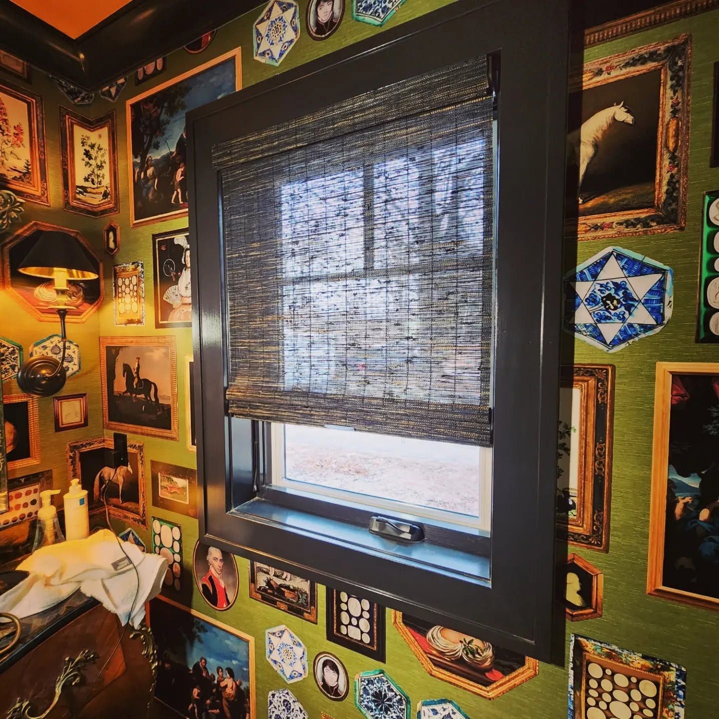 Cozy room with a window, woven shade, and walls covered in framed photos and colorful memorabilia