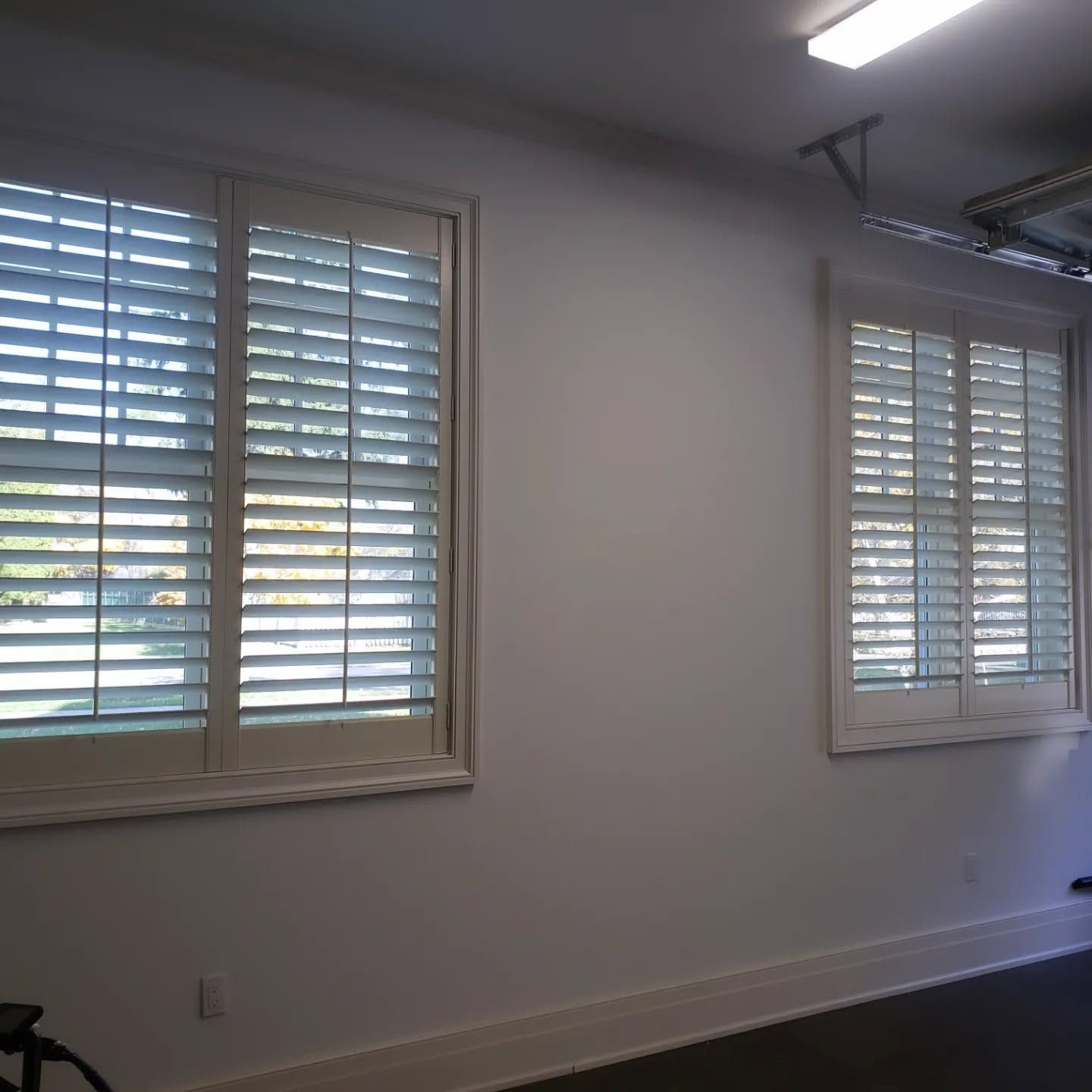 Empty room with white walls, two shuttered windows, and dark hardwood floors