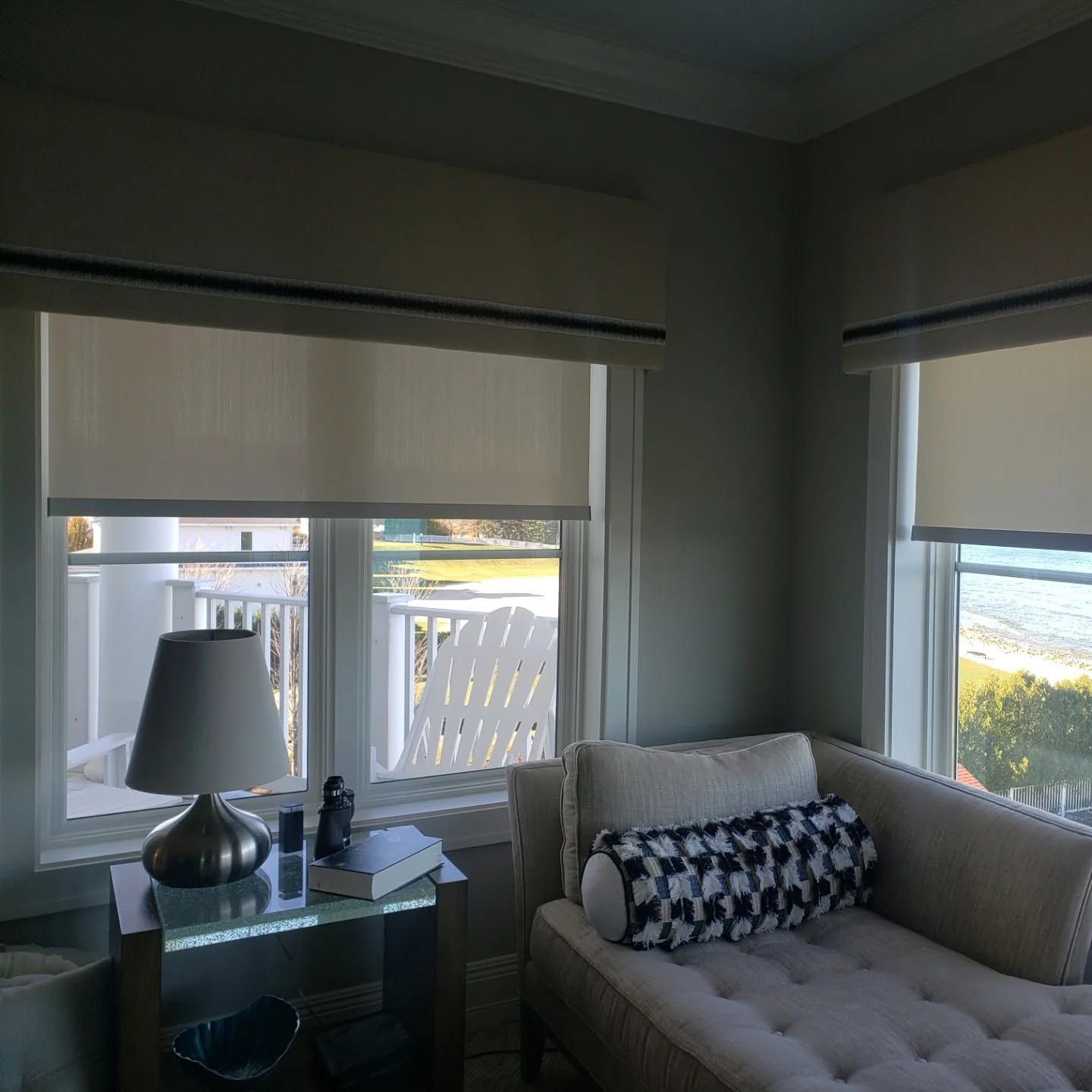 Cozy living room corner with sofa, side table, lamp, and large windows overlooking the beach
