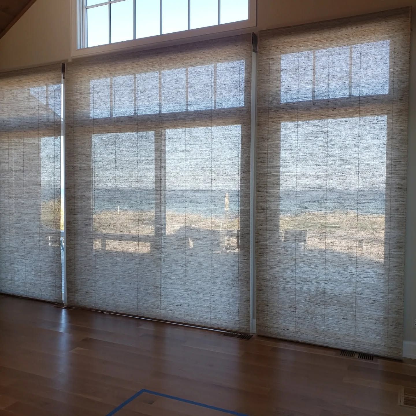 Sunlit room with tall windows and sheer curtains overlooking a distant landscape