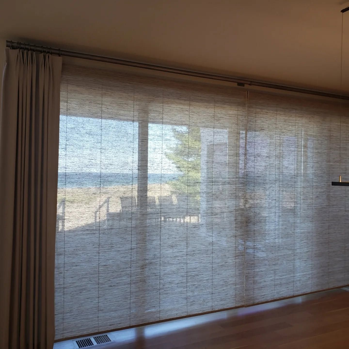 Living room with woven blinds over large sliding glass doors, showing a beach and patio outside