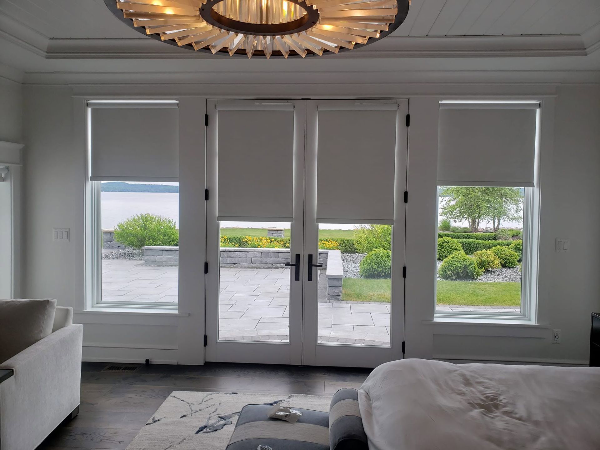 Modern living room with white walls, chandelier, large glass doors, and a view of a patio and greenery outside
