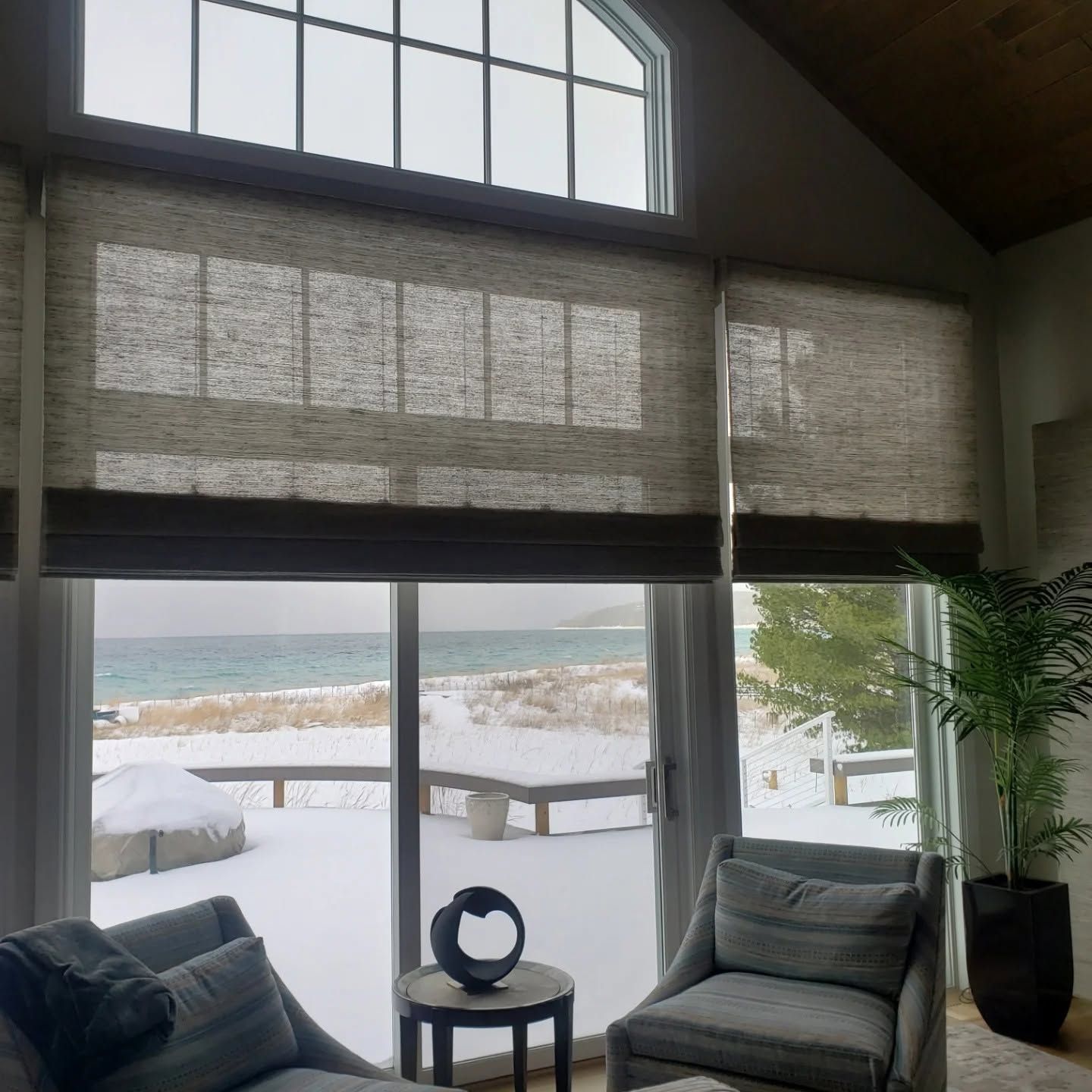 Snowy lake view through large windows in a cozy room with two gray chairs and a round table.
