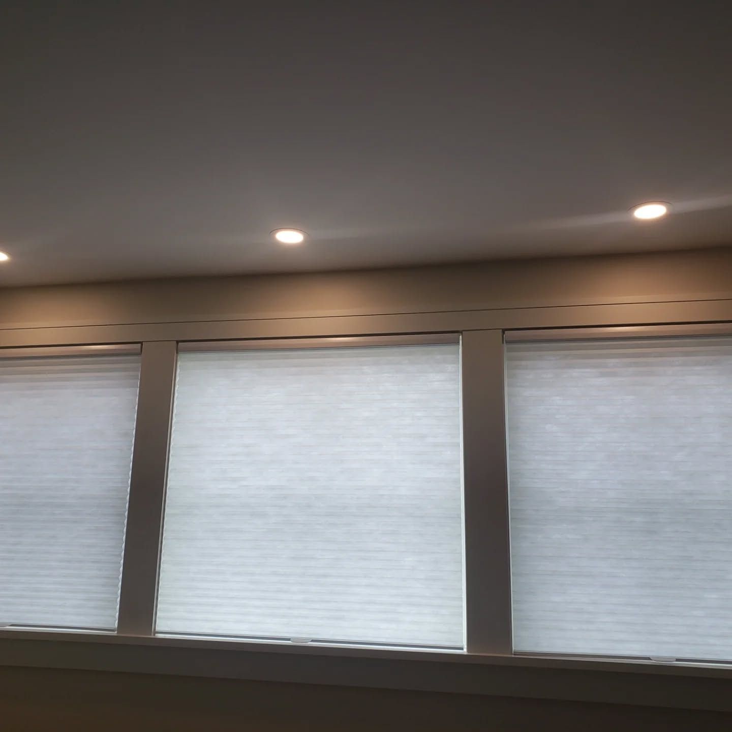 Three bright window shades beneath a ceiling with recessed lights