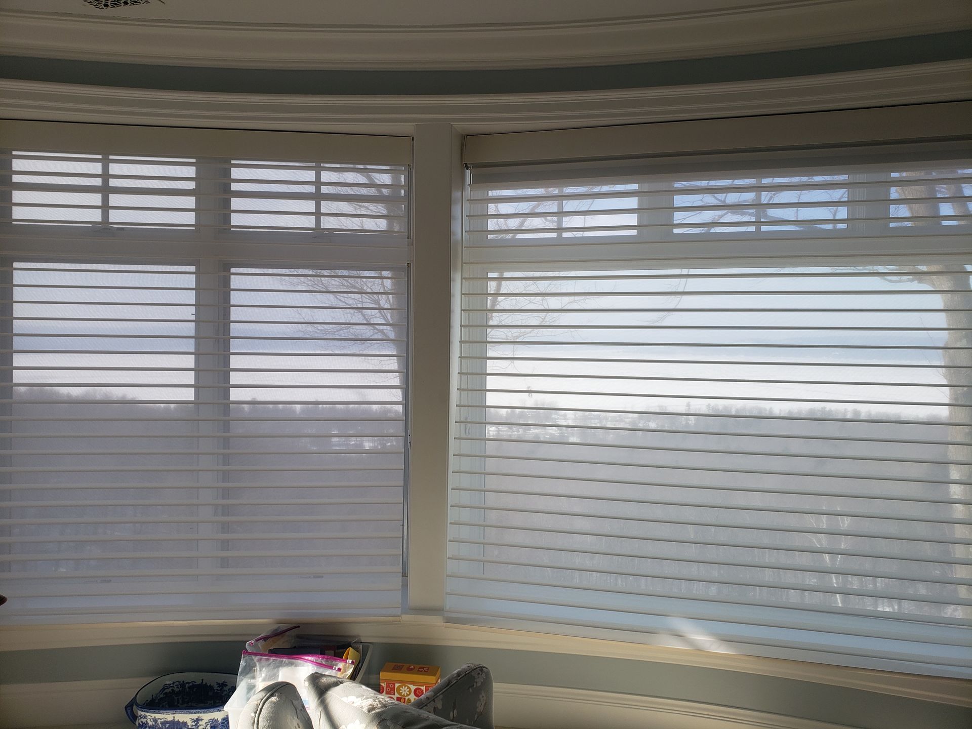Window blinds with daylight streaming in above a cluttered shelf or bin in a room