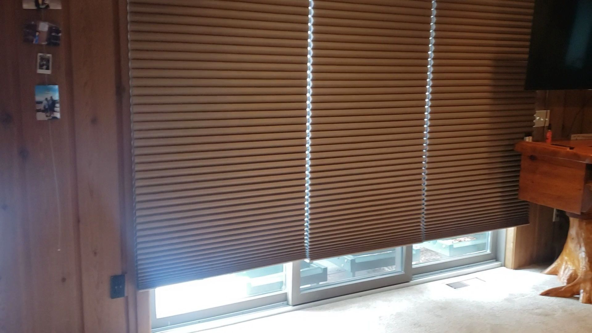 Brown blinds cover a window in a wood-paneled room, with light showing through the bottom.