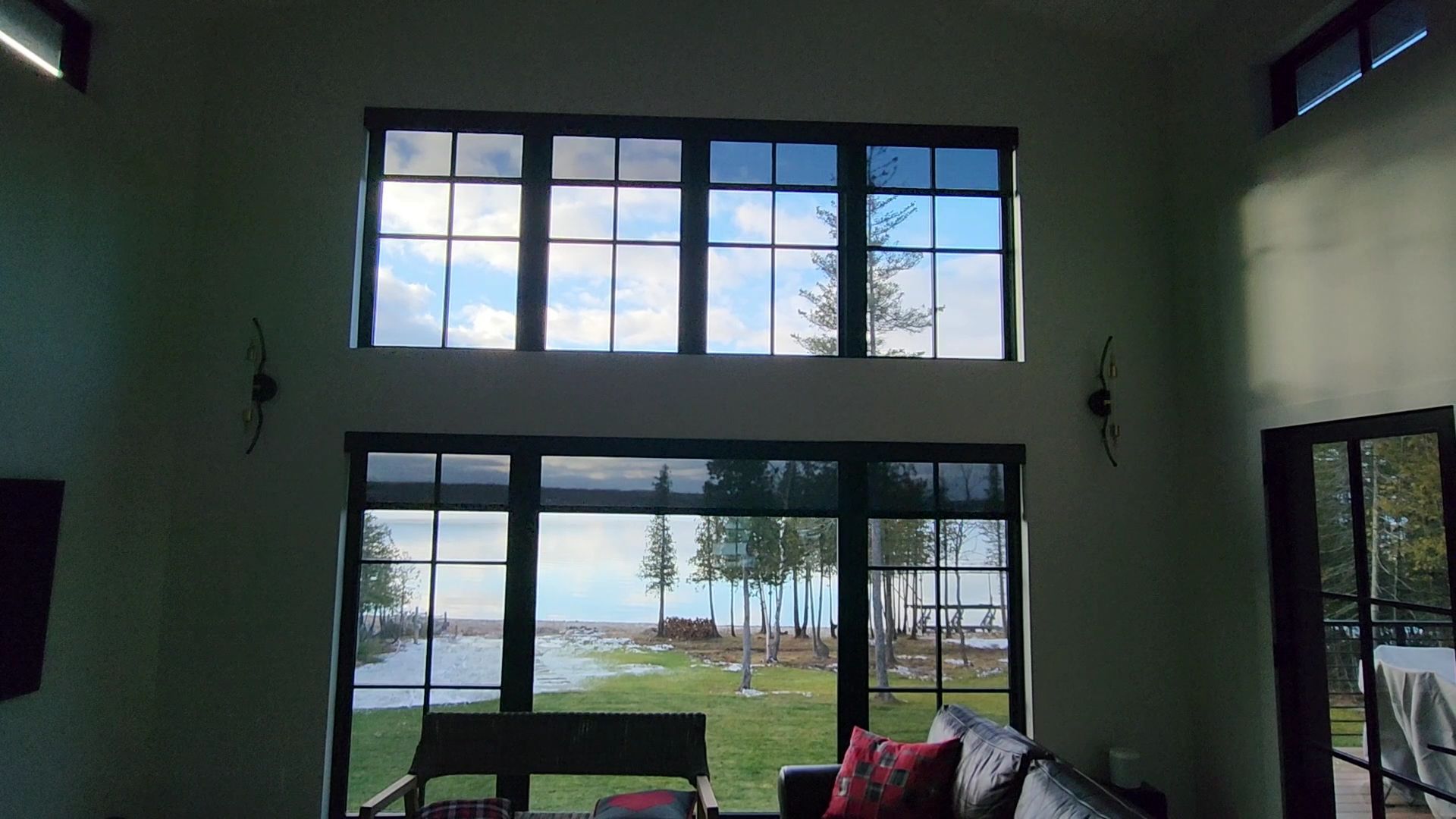 Living room with large windows overlooking a lake and trees at dusk