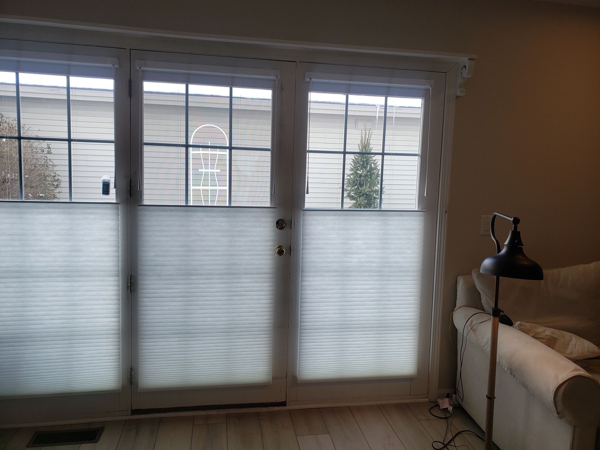 Living room with large sliding glass doors, white blinds, and a beige sofa with a black lamp.