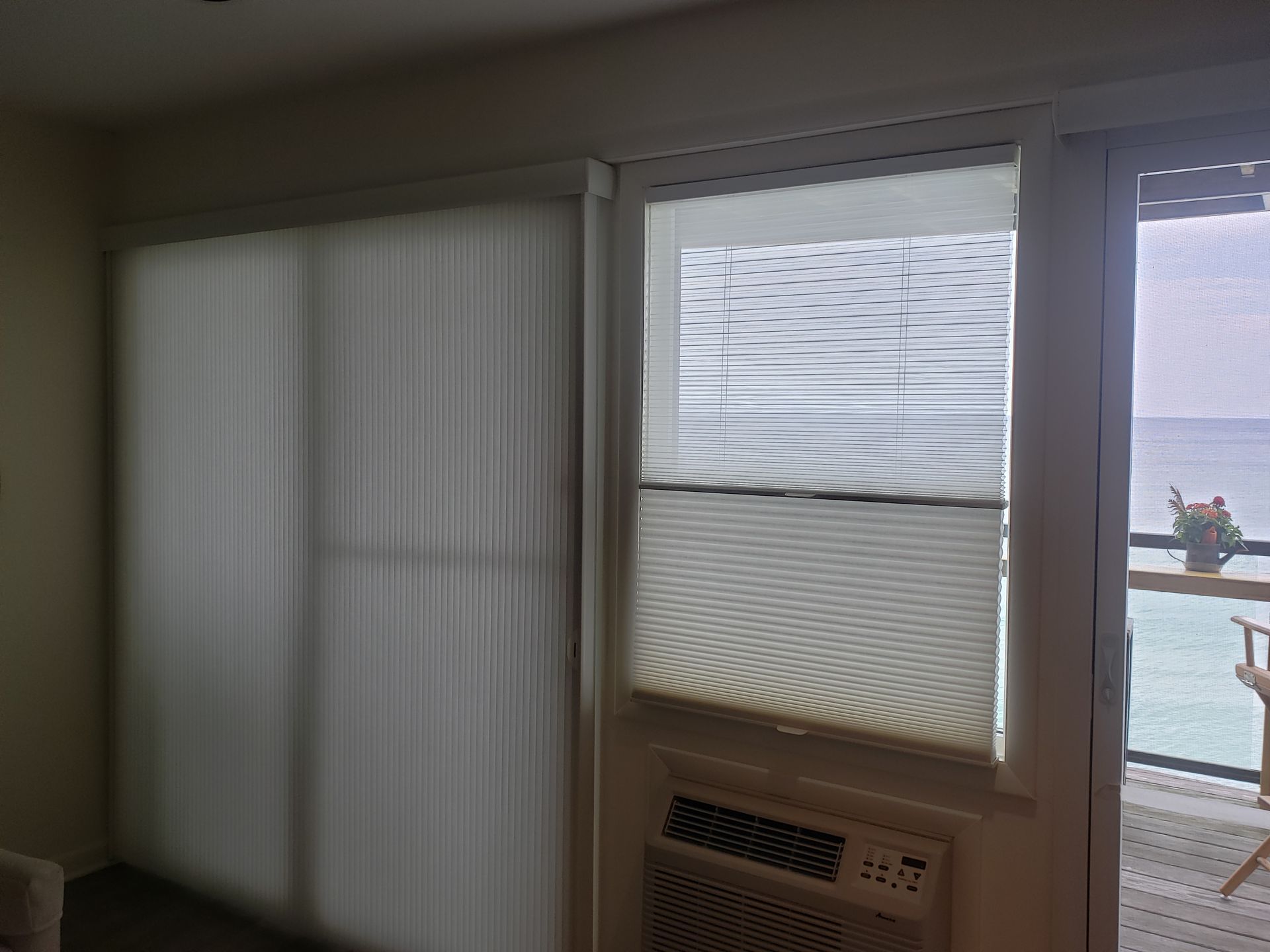 Interior with vertical blinds, window air conditioner, and a view of the ocean through a partially open window