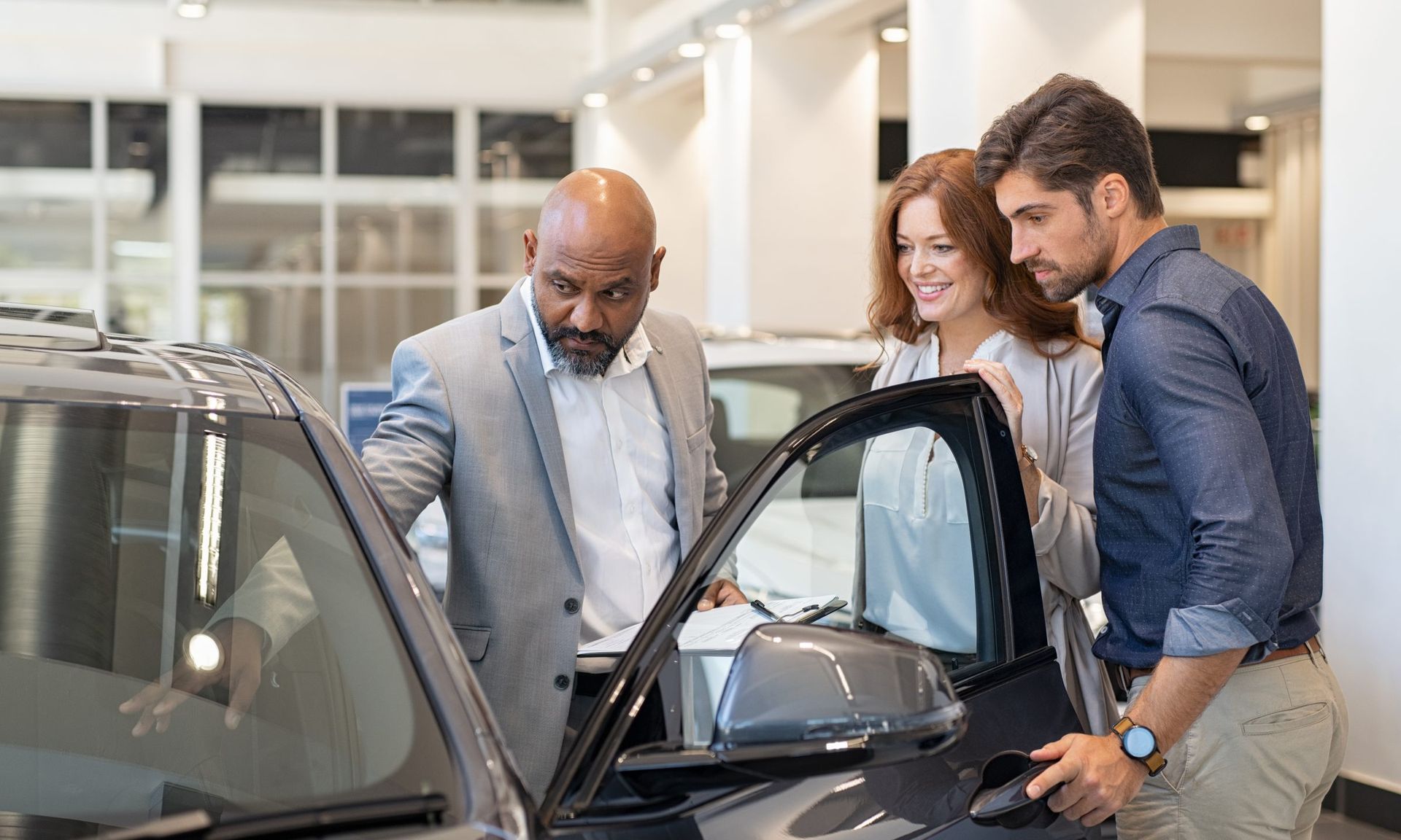 three individuals look inside a used car being sold
