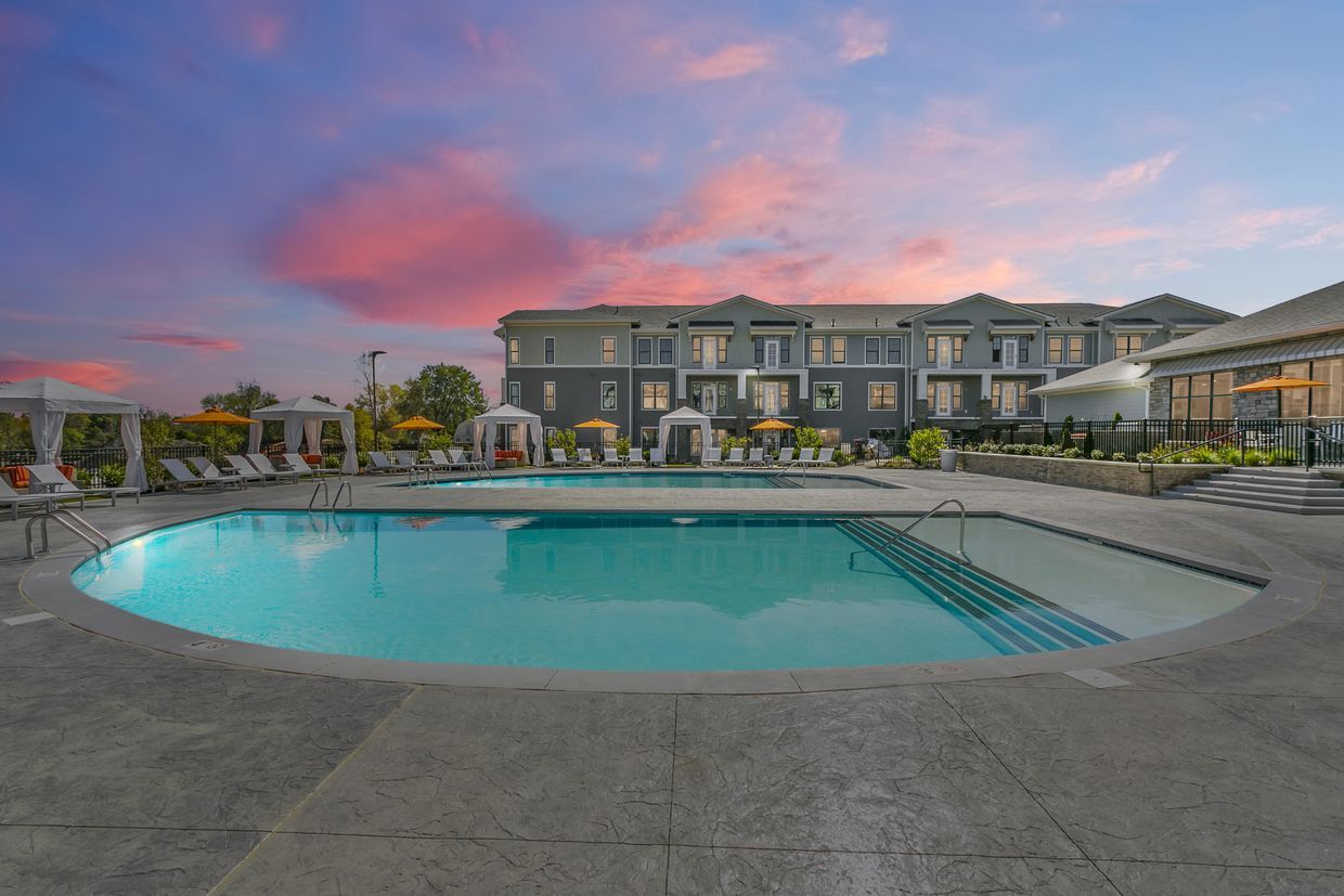 Swimming pool in front of a multi-story building at sunset; clouds of pink and blue.