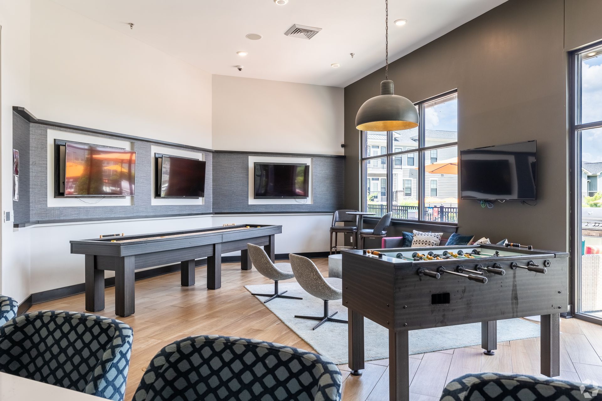 Modern game room with pool table, ping-pong table, wall TVs, and large windows.
