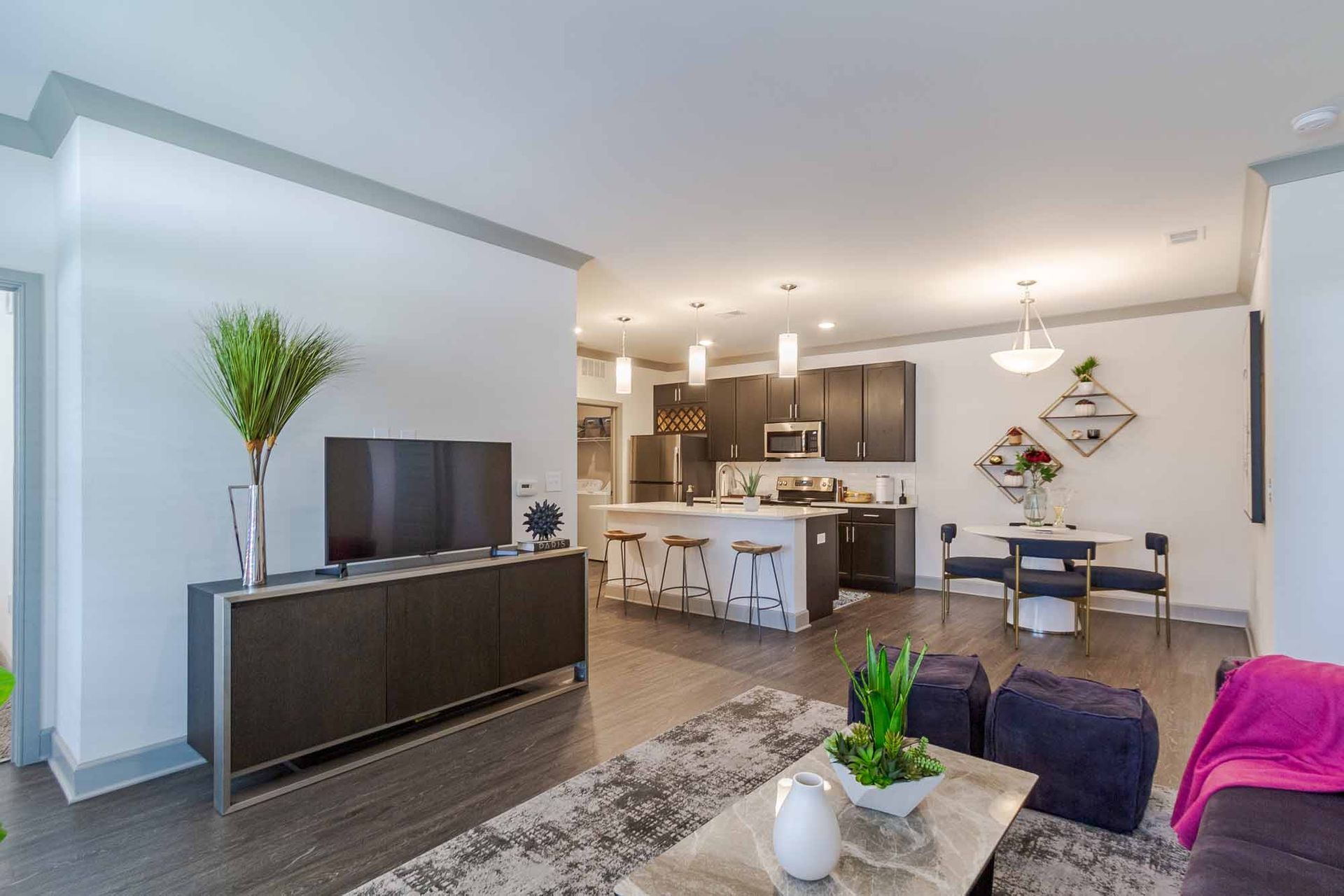Modern open-plan living space with kitchen and dining area; gray walls, dark wood accents, and light-colored furniture at Haven on Tucker Apartments in Louisville, KY