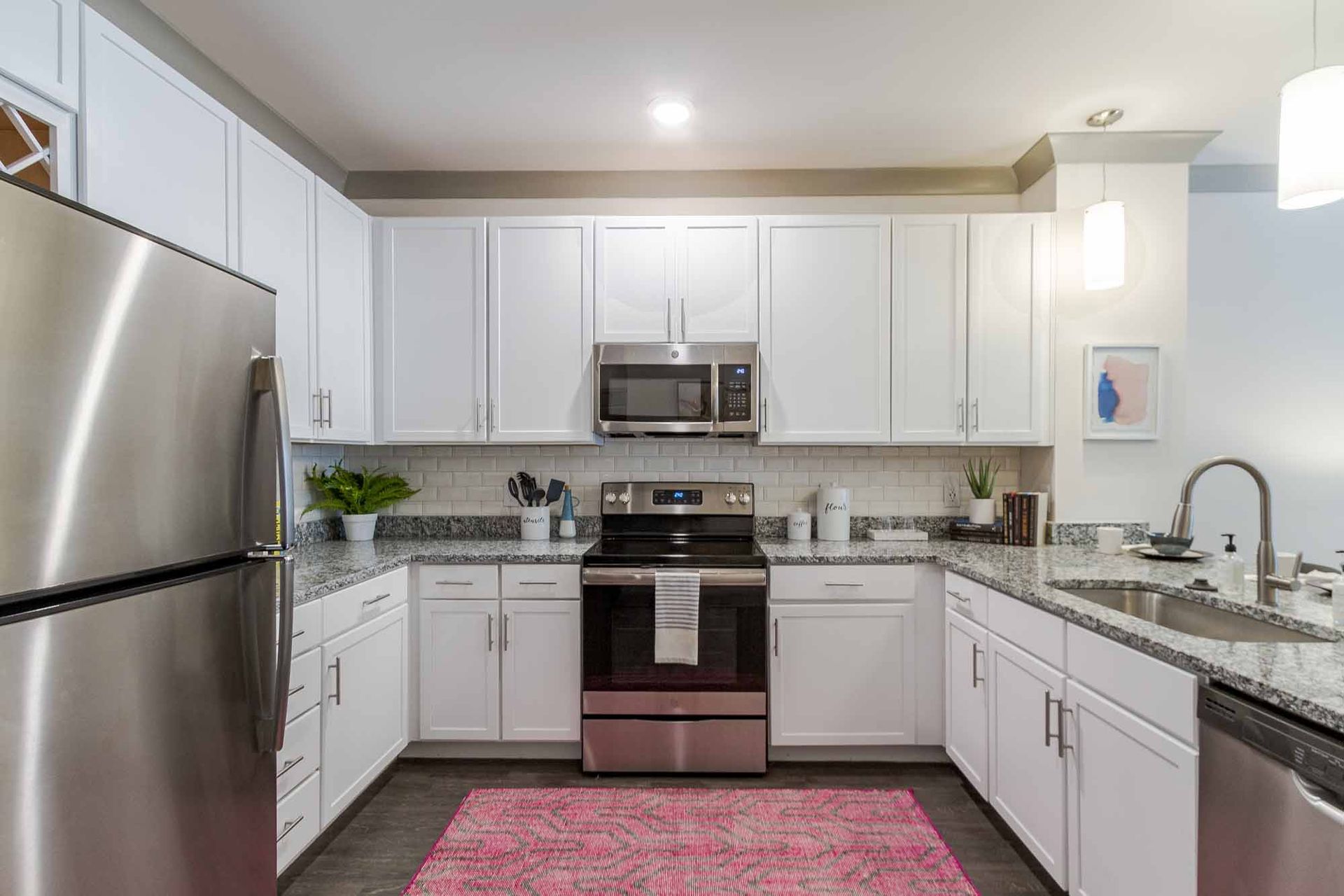 Modern white kitchen with stainless steel appliances, granite countertops, and a pink rug at Haven on Tucker Apartments in Louisville, KY