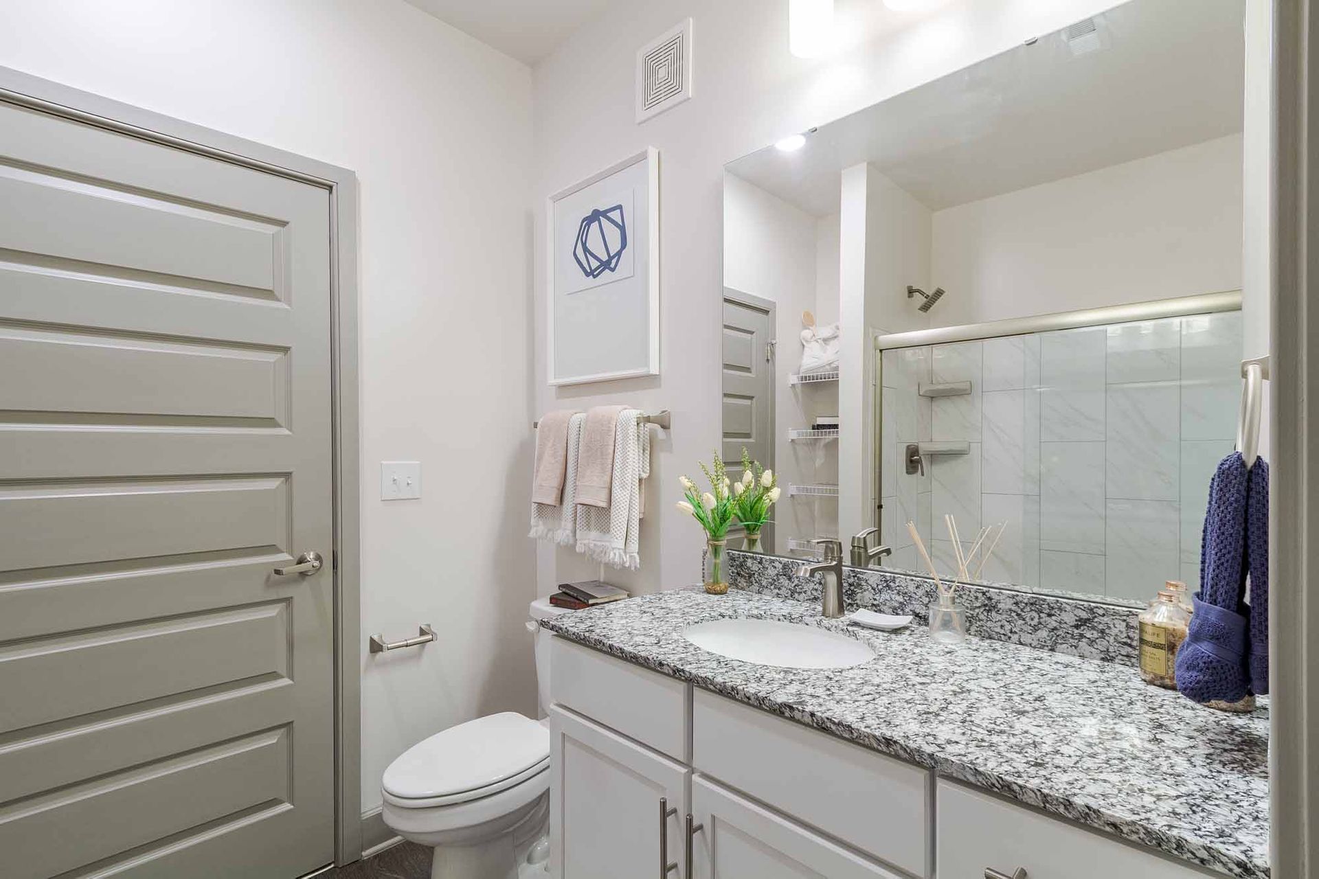 Bathroom with white vanity, gray granite countertop, toilet, mirror, and shower at Haven on Tucker Apartments in Louisville, KY