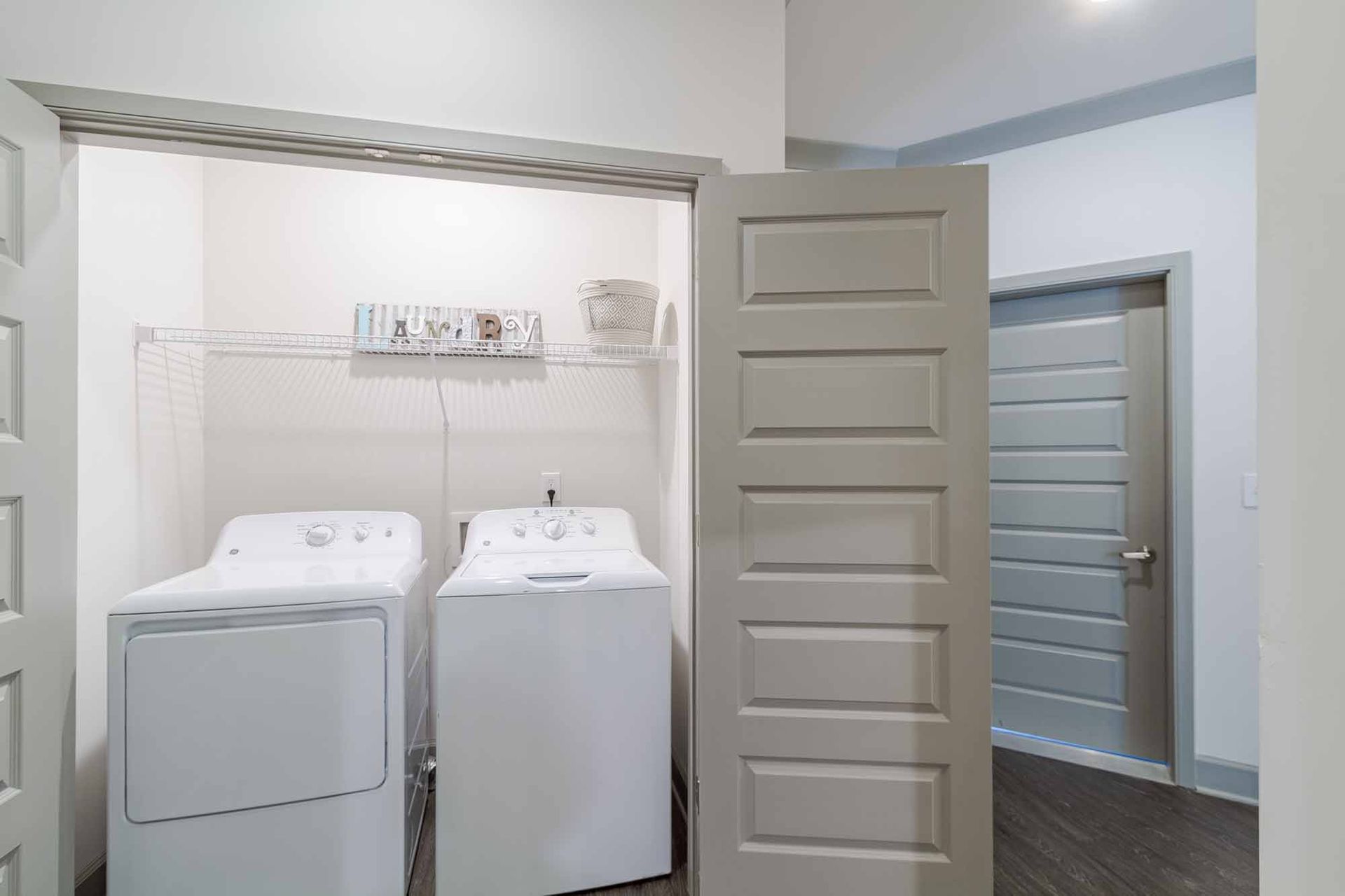 Laundry room with white washer and dryer, open door, and adjacent door at Haven on Tucker Apartments in Louisville, KY