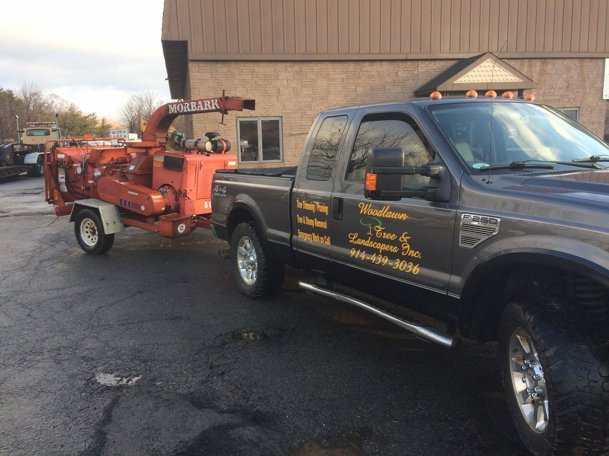 Truck towing an orange wood chipper; parked in front of a building.
