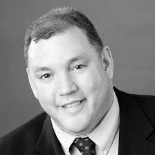 Black-and-white headshot of a smiling man in a suit and tie.