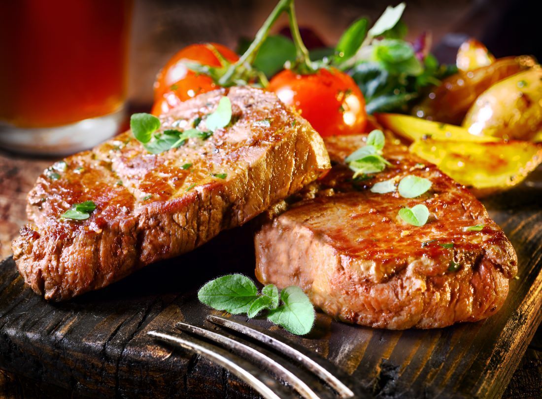 Two Steaks and Vegetables on a Wooden Cutting Board With a Fork — Prime Meats NT in Coconut Grove, NT