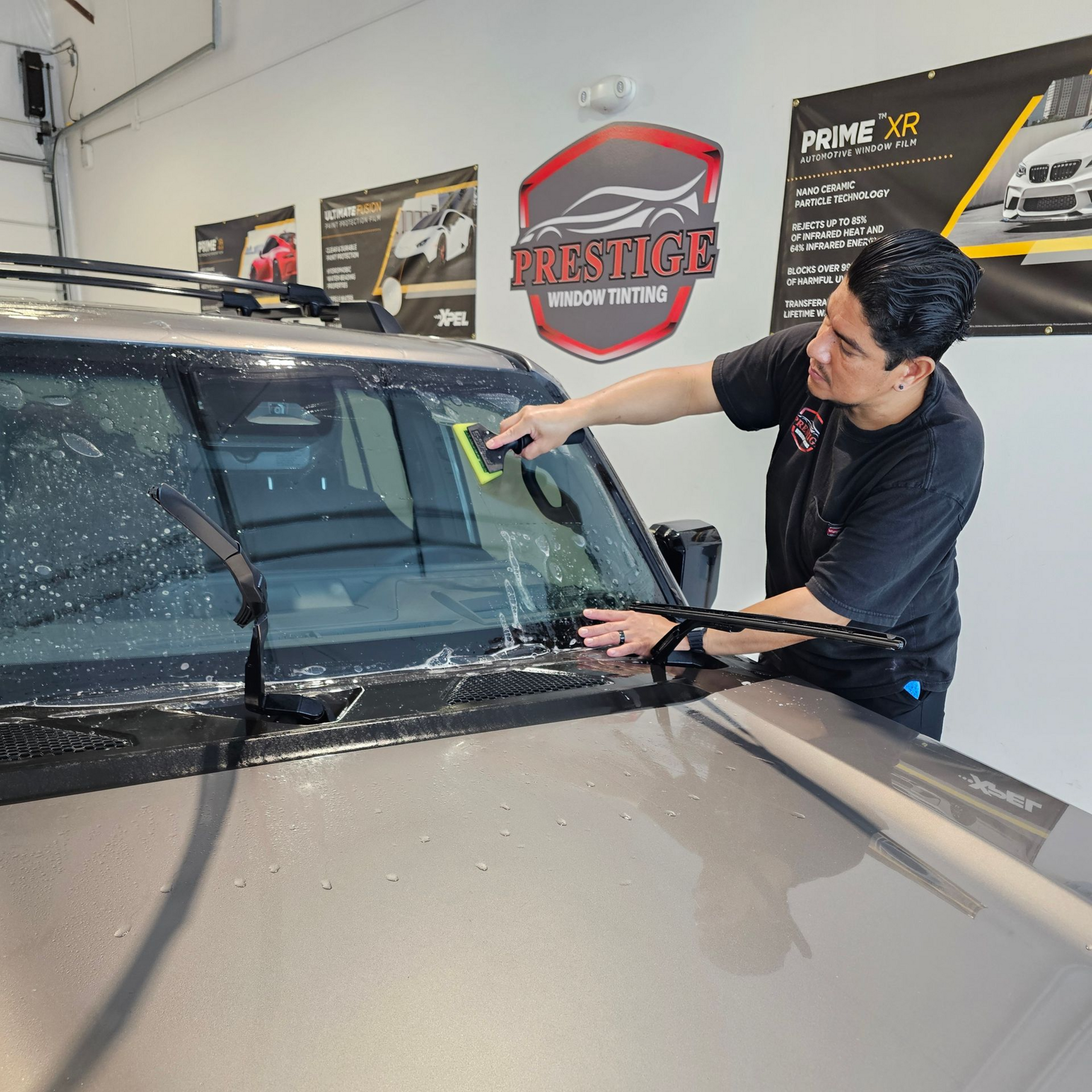 Person cleaning a car windshield with a squeegee in an auto detailing shop