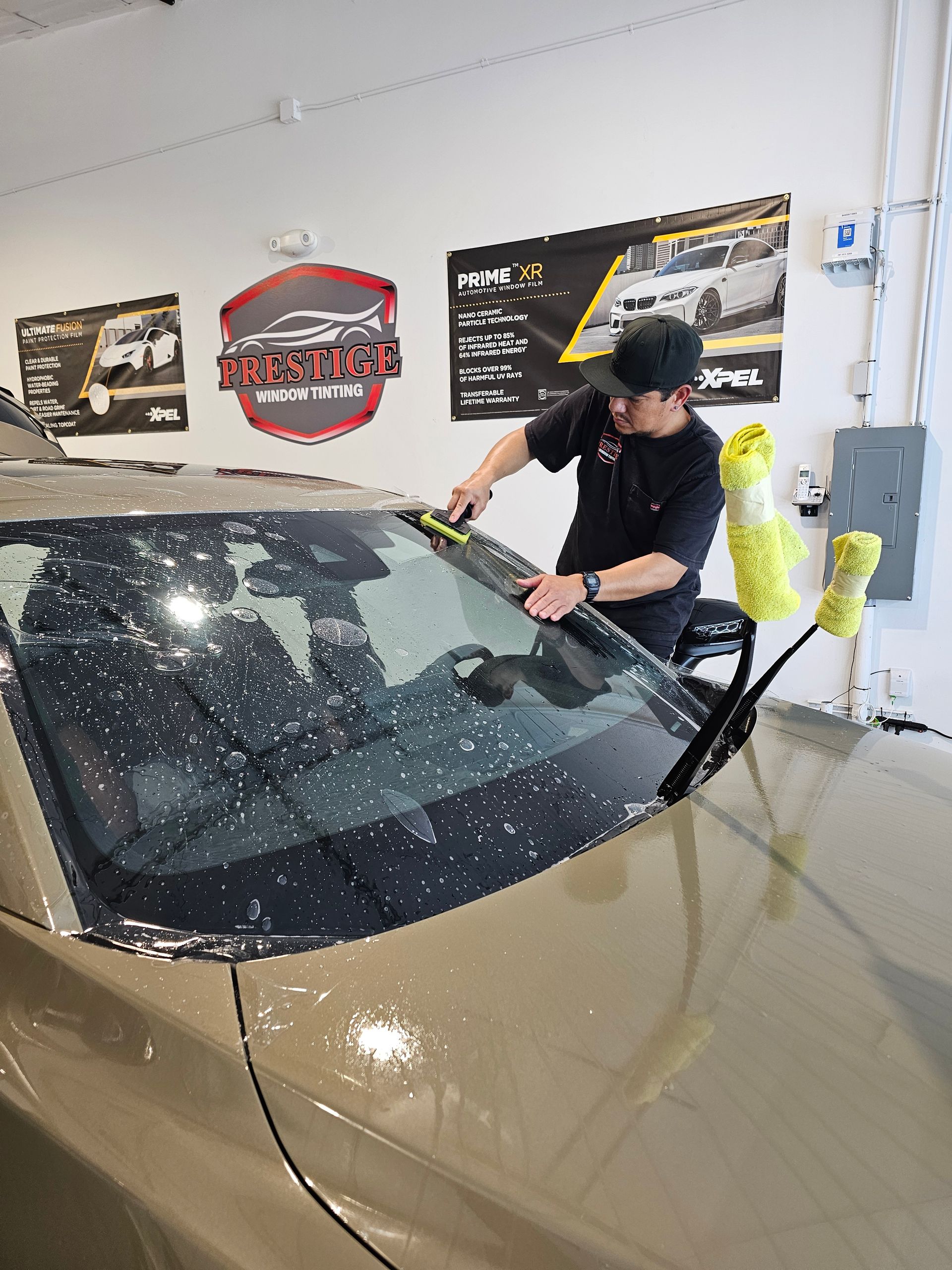 A man is applying window tinting to a blue car.