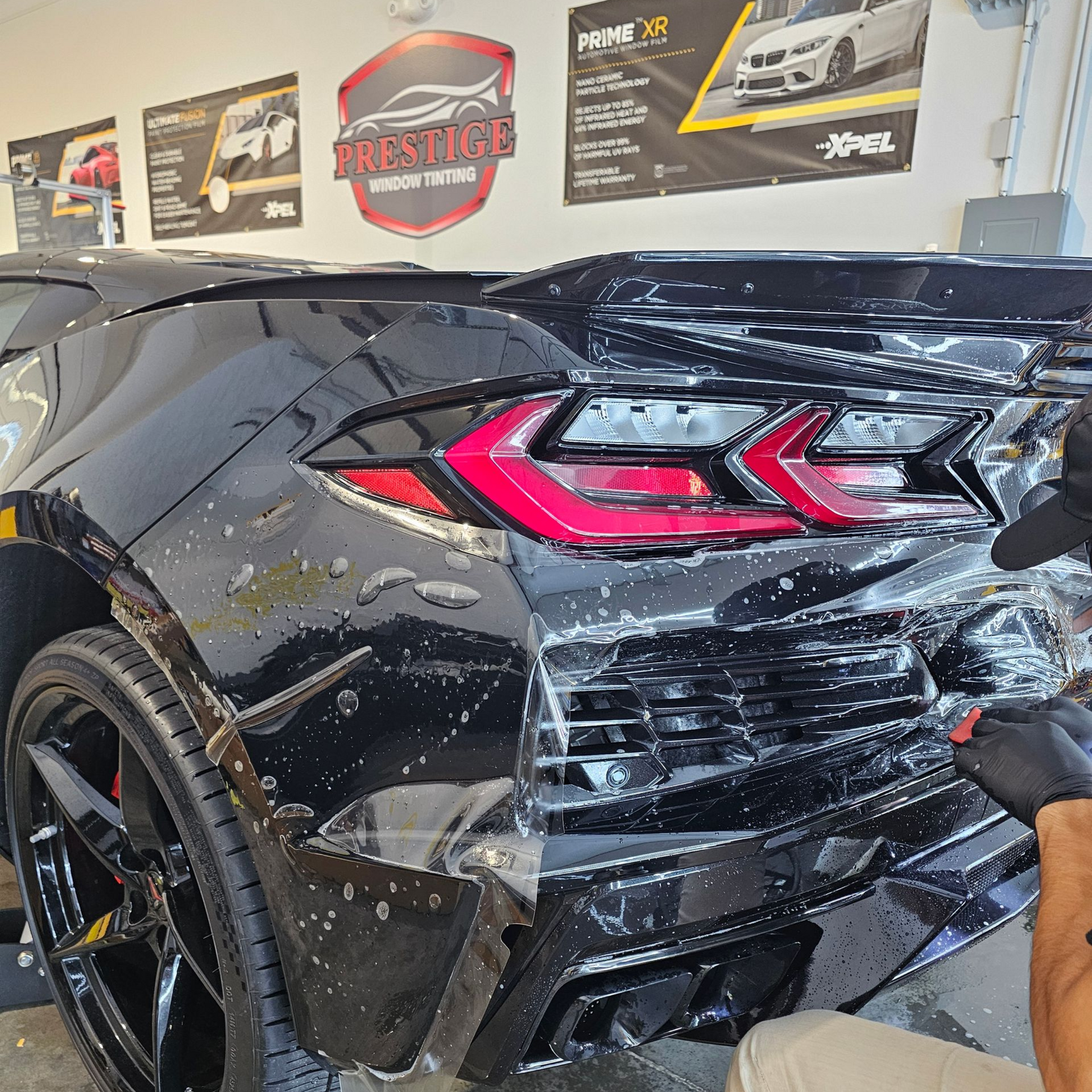 Black sports car rear quarter with damaged bumper and taillight in an indoor auto shop