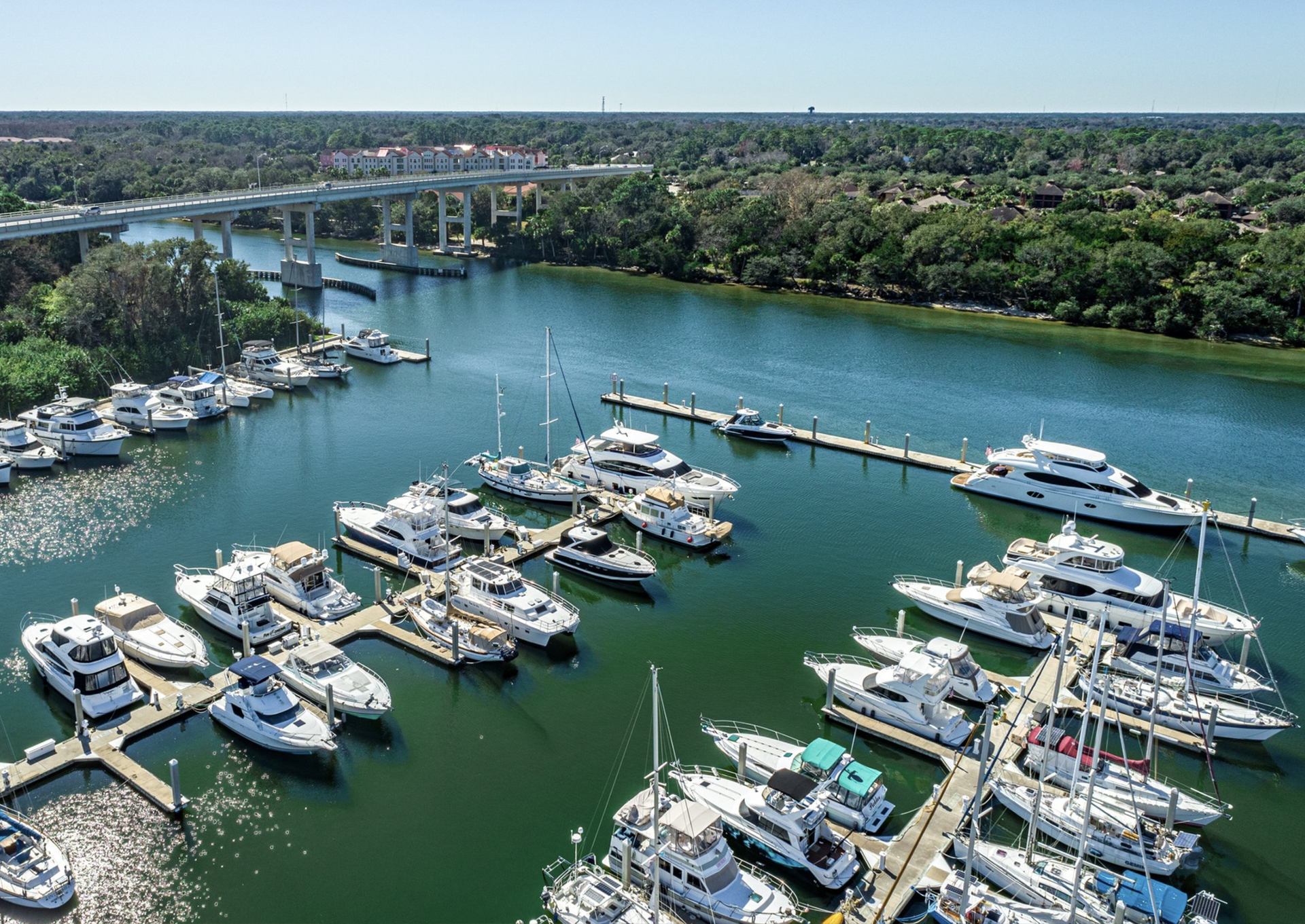 An aerial view of a marina filled with boats and a bridge in the background.