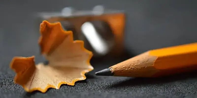 Close-up of sharpened orange pencils with curled wood shavings on a dark surface