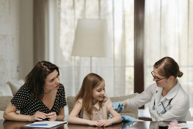 Caregiver using a stethoscope to listen to a child’s back while they sit on a bed