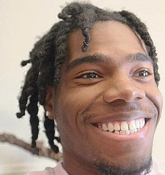 Close-up of a smiling person with twisted hair, looking off to the side indoors.