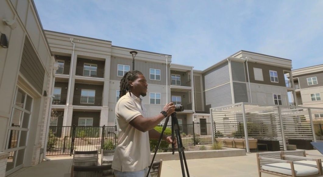 Person adjusting a camera tripod in a courtyard of modern apartment buildings.
