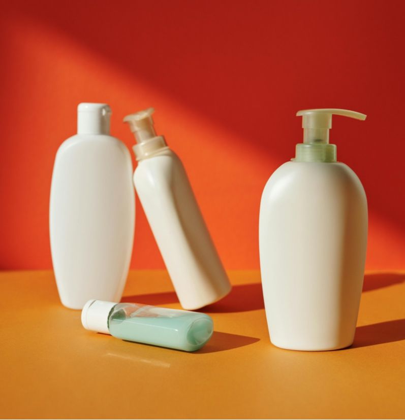 Four white lotion bottles on an orange surface against a red background, one lying on its side.