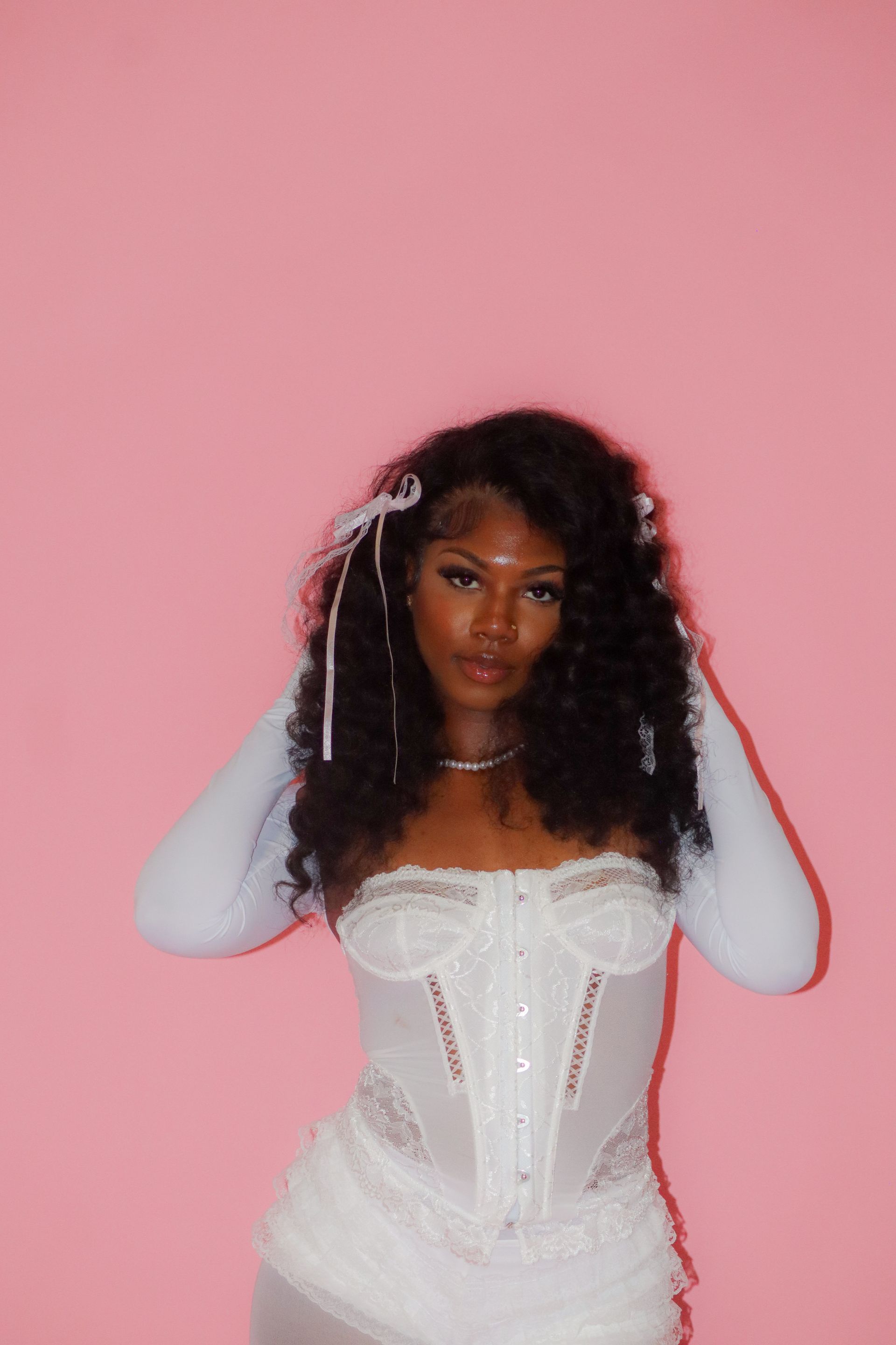 Woman in a white corset dress posing against a pink wall