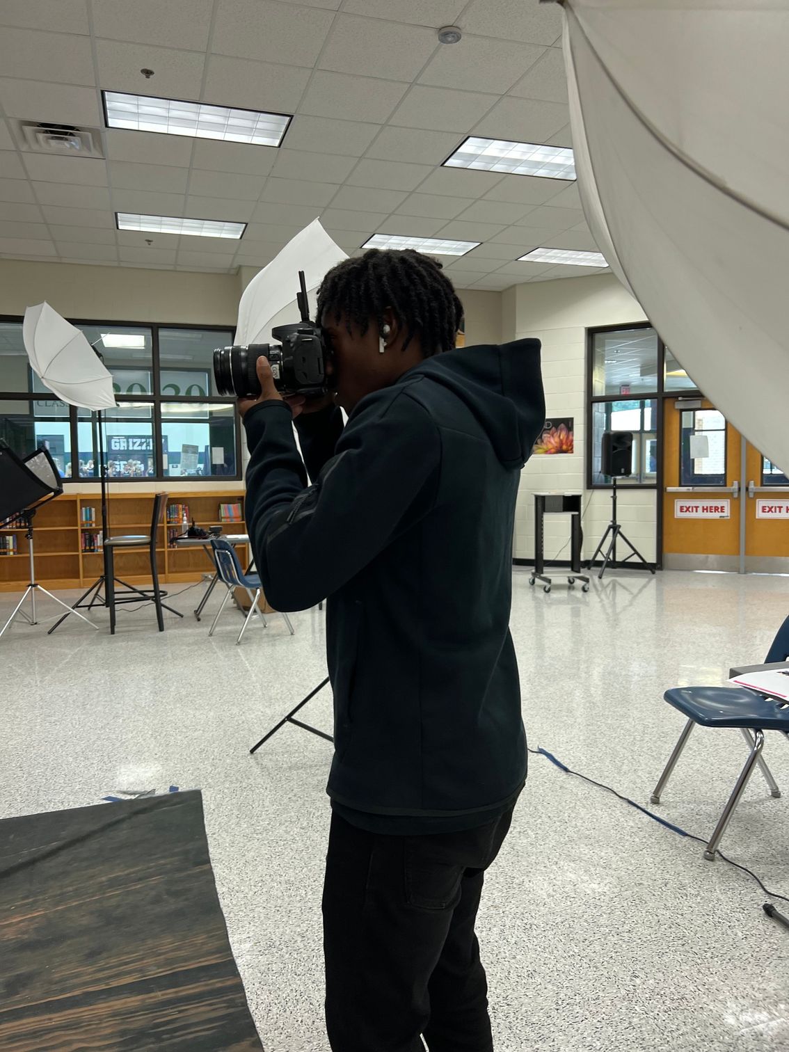 Person holding a camera in a bright indoor room with folding chairs and photo lighting equipment