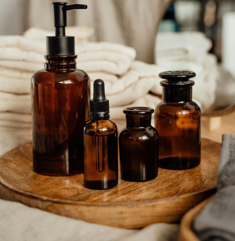 Amber glass bath bottles on a wooden tray with folded towels in the background