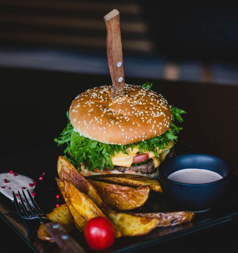 Gourmet burger with sesame bun, fries, cherry tomato, and dipping sauce on a black plate