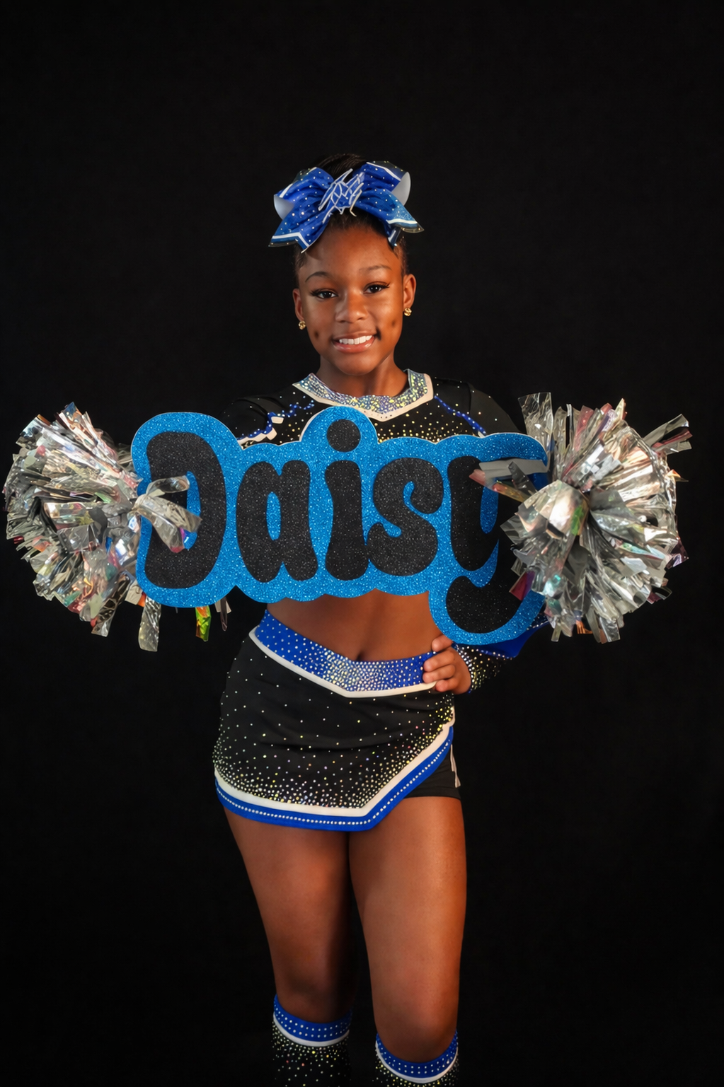 Cheerleader in black-and-blue uniform holding silver pom-poms with “Daisy” sign on a dark background