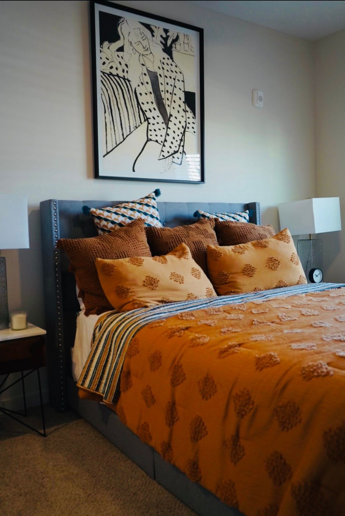 Neatly made bed with orange patterned bedding and pillows in a modern bedroom with wall art.