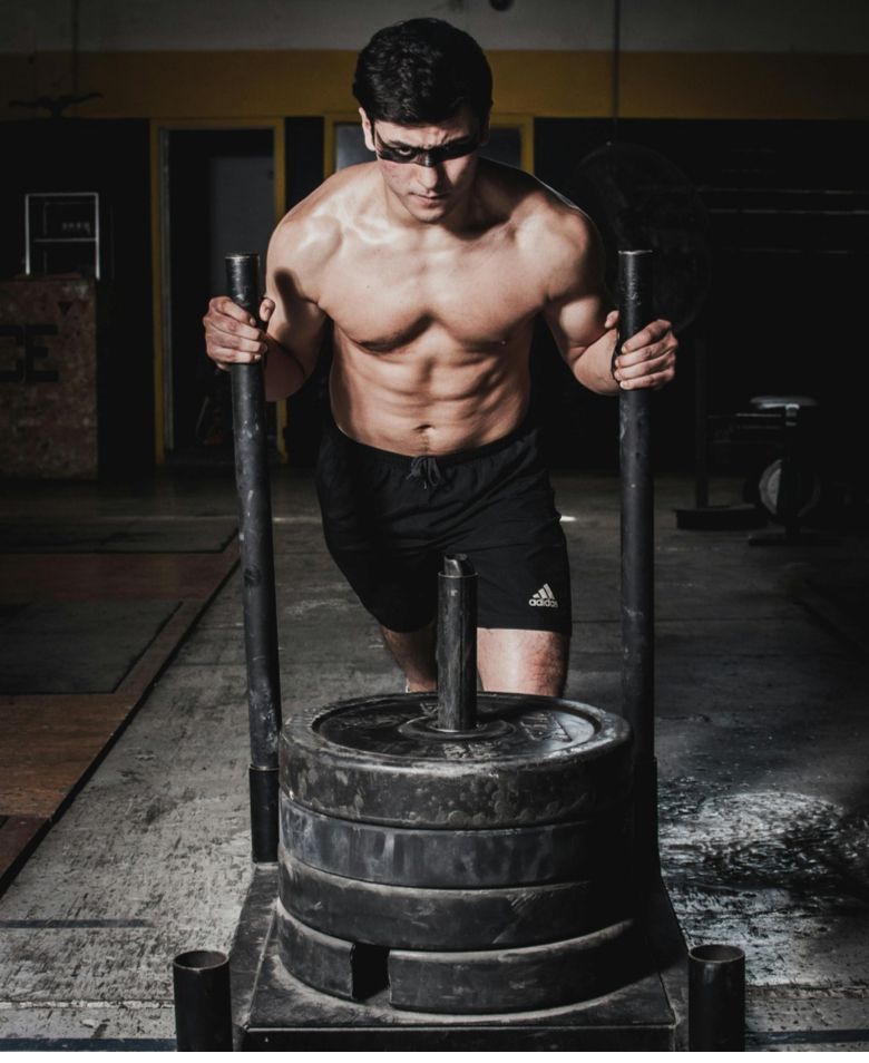 Muscular man pushing a weighted sled in a dim gym, focused on strength training