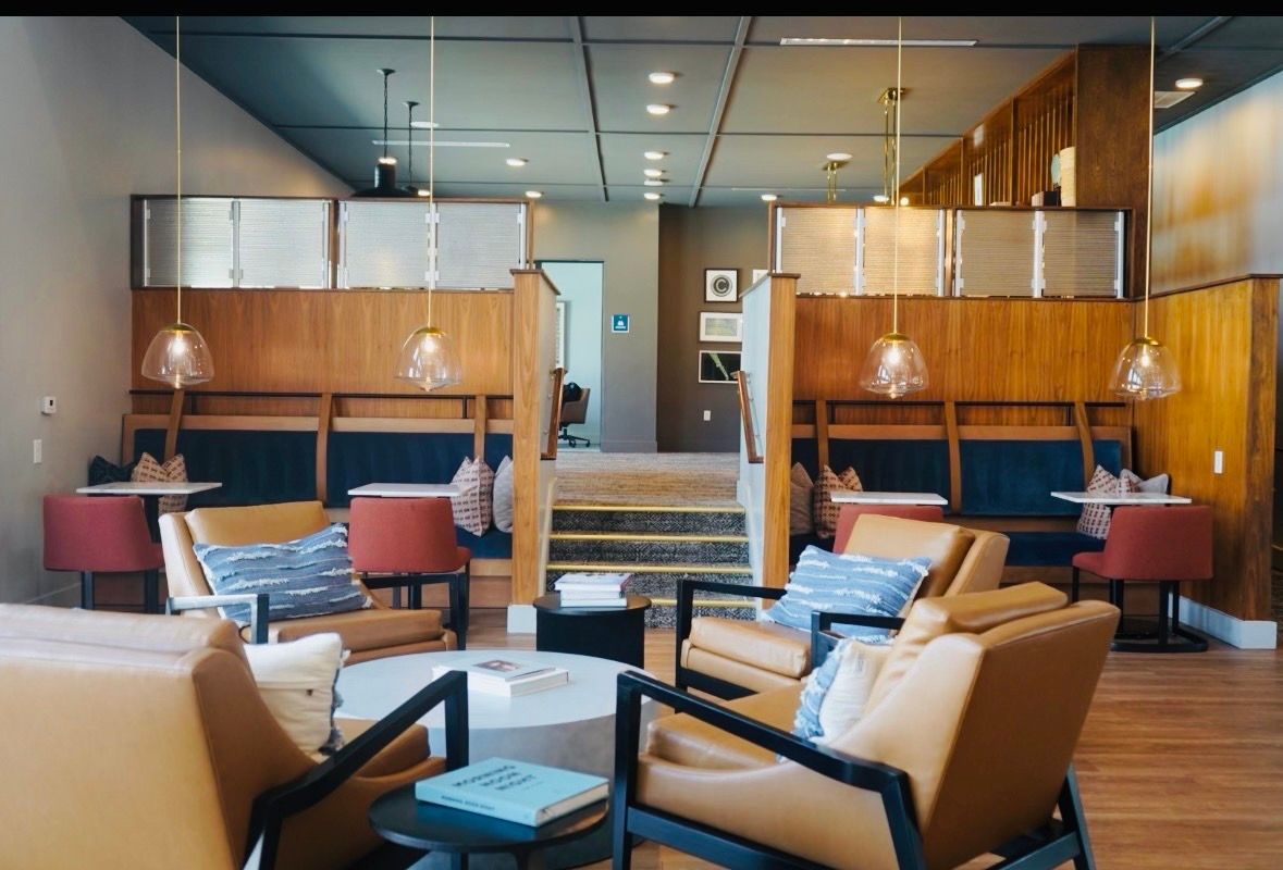 Modern hotel lobby with tan chairs, red side tables, wood paneling, and central staircase